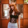 Redhead woman with red hair, posh rose tinted sunglasses, standing in front of a beautiful window pane