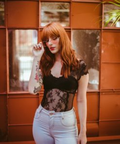 Redhead woman with red hair, posh rose tinted sunglasses, standing in front of a beautiful window pane