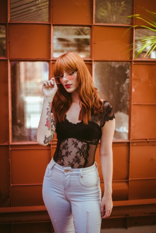 Redhead woman with red hair, posh rose tinted sunglasses, standing in front of a beautiful window pane