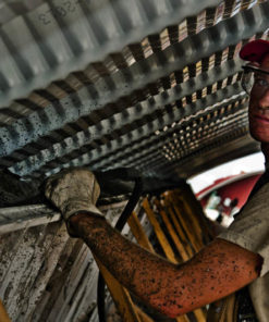 Hard-working man working on industrial building, with red hat, t-shirt, covered in dirt, gloves, harness