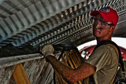 Hard-working man working on industrial building, with red hat, t-shirt, covered in dirt, gloves, harness