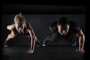 Woman and man doing one-arm pushups on a dark background